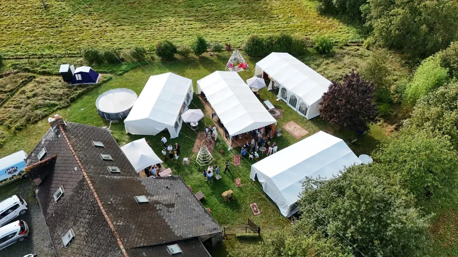 Plusieurs tentes blanches installées autour d'une ferme, vue aérienne