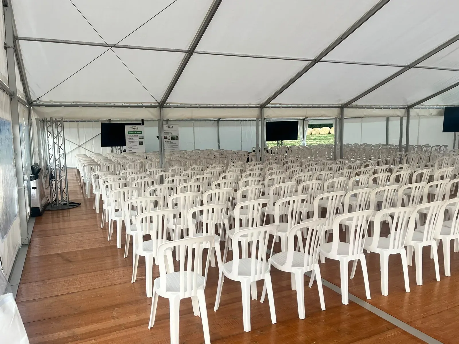 Rangées de chaises blanches sur plancher sous un chapiteau, pour une cérémonie