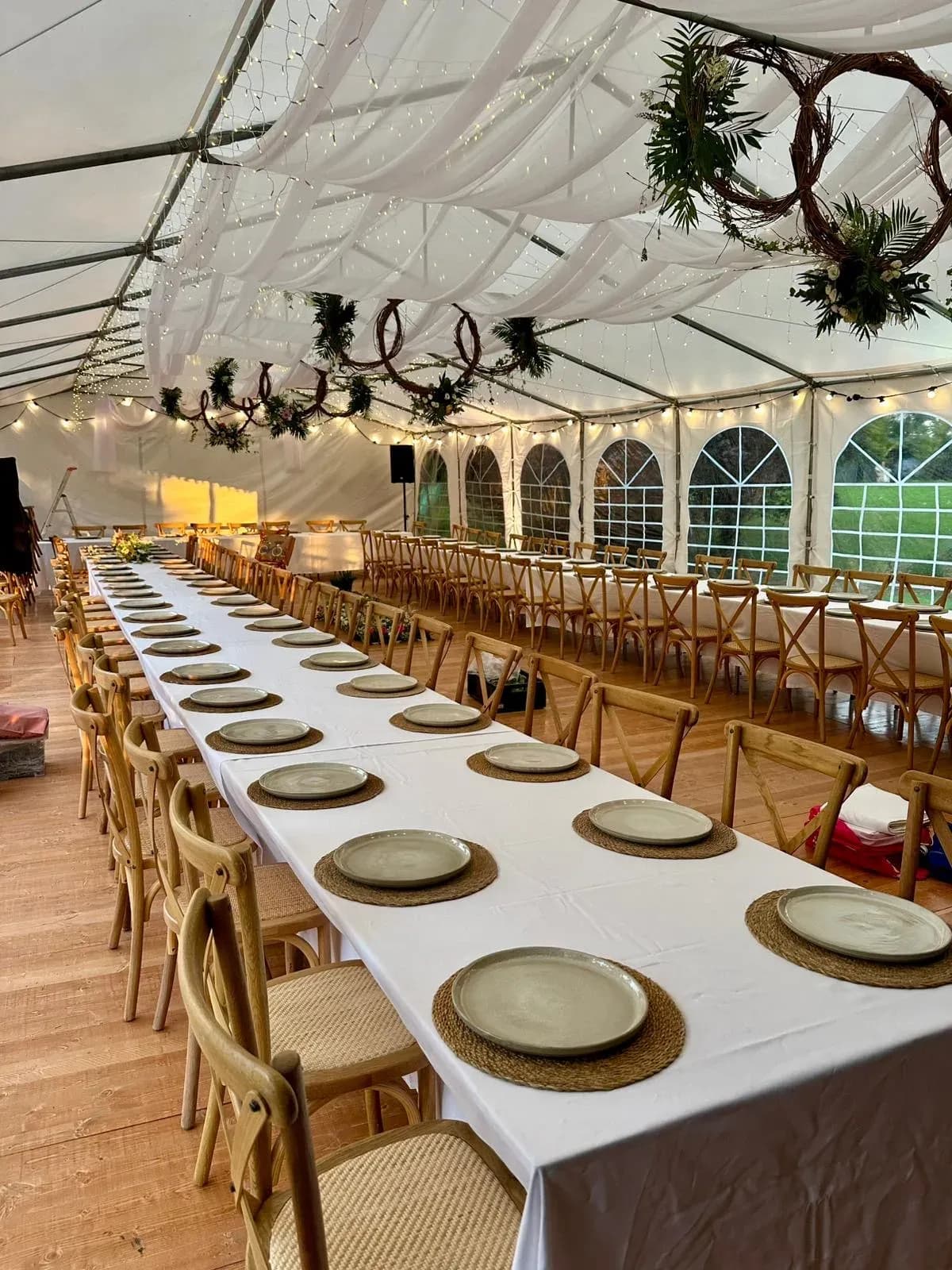 Intérieur d'un chapiteau de mariage, longues tables dressées et couronnes végétales suspendues