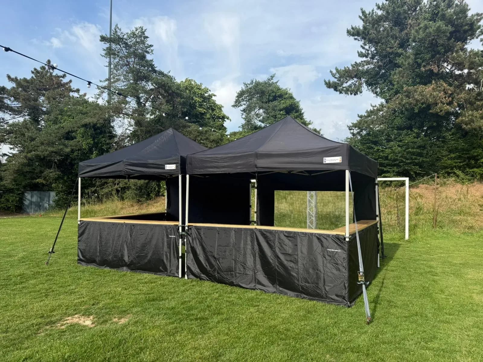 Tente pliante noire montée sur une pelouse, pour un stand ou une buvette